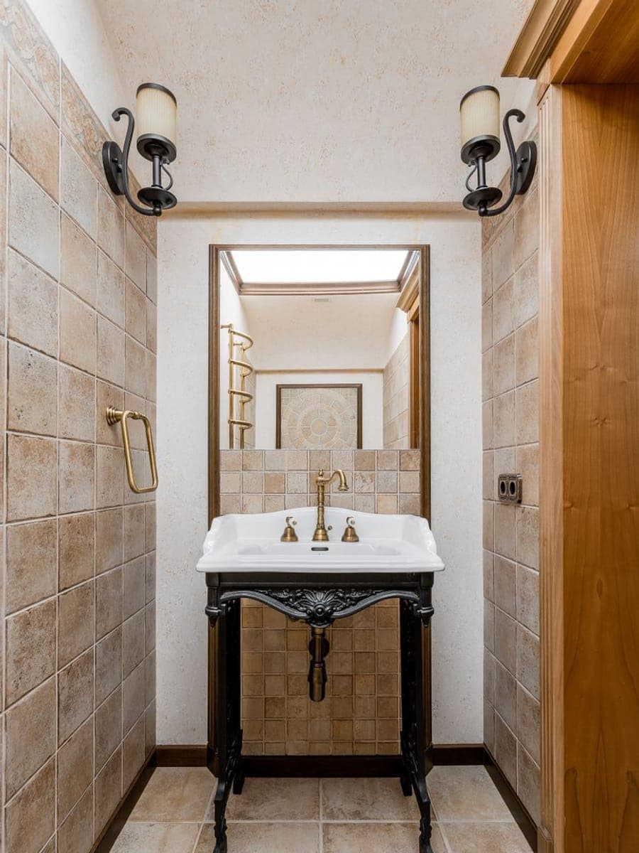 Lavabo de porcelana sobre un pie de hierro fundido, con grifería de latón, espejo y apliques en un aseo alicatado