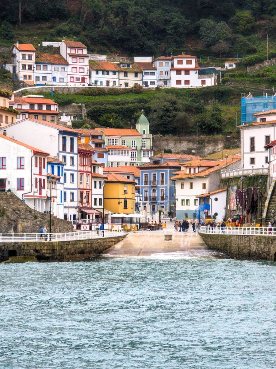 Pueblo marinero de casas de colores escalonadas sobre un puerto, con el agua verde en primer término