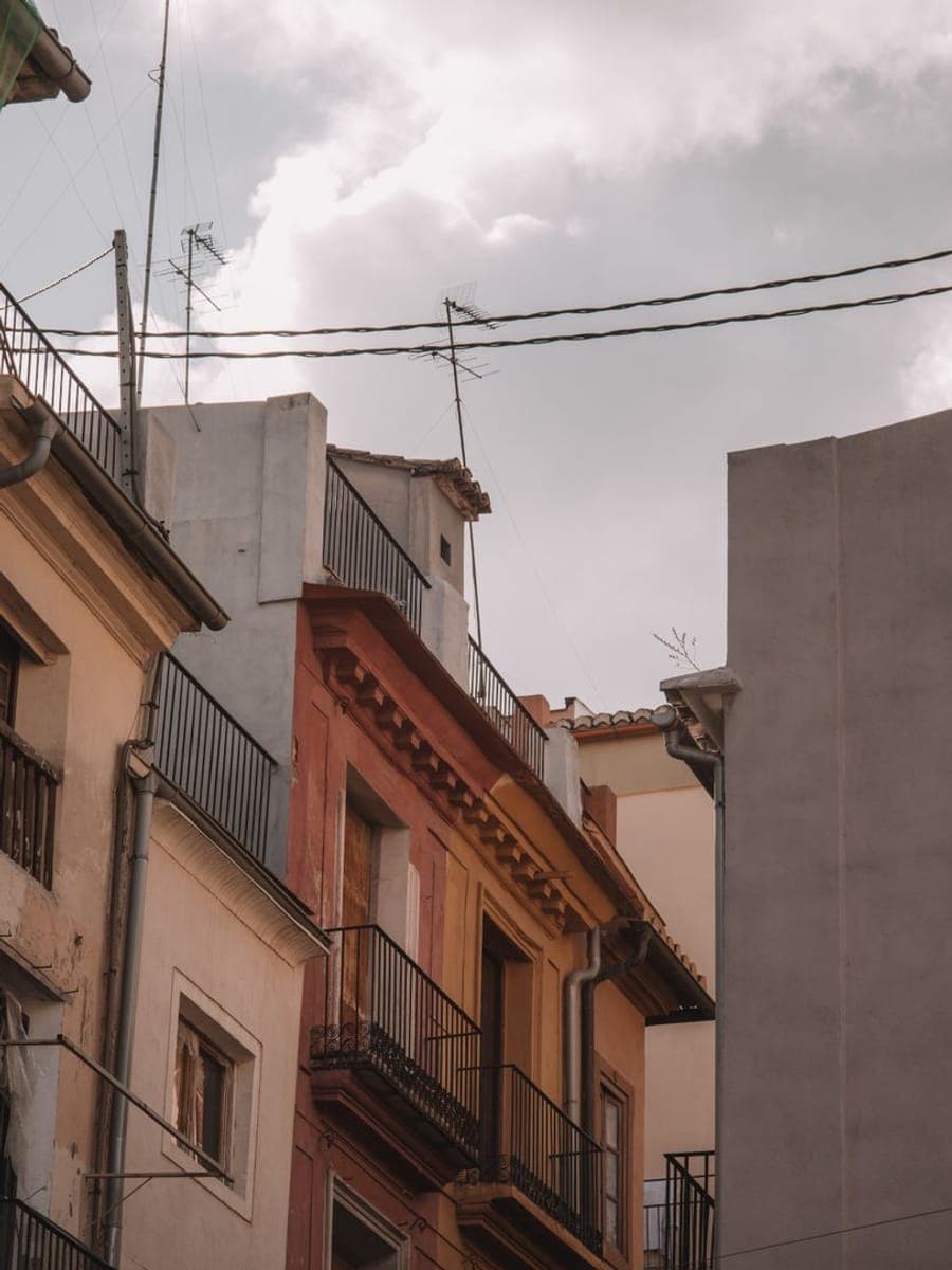 Fachadas y tejados de un casco antiguo con antenas, canalones y balcones de forja bajo un cielo encapotado