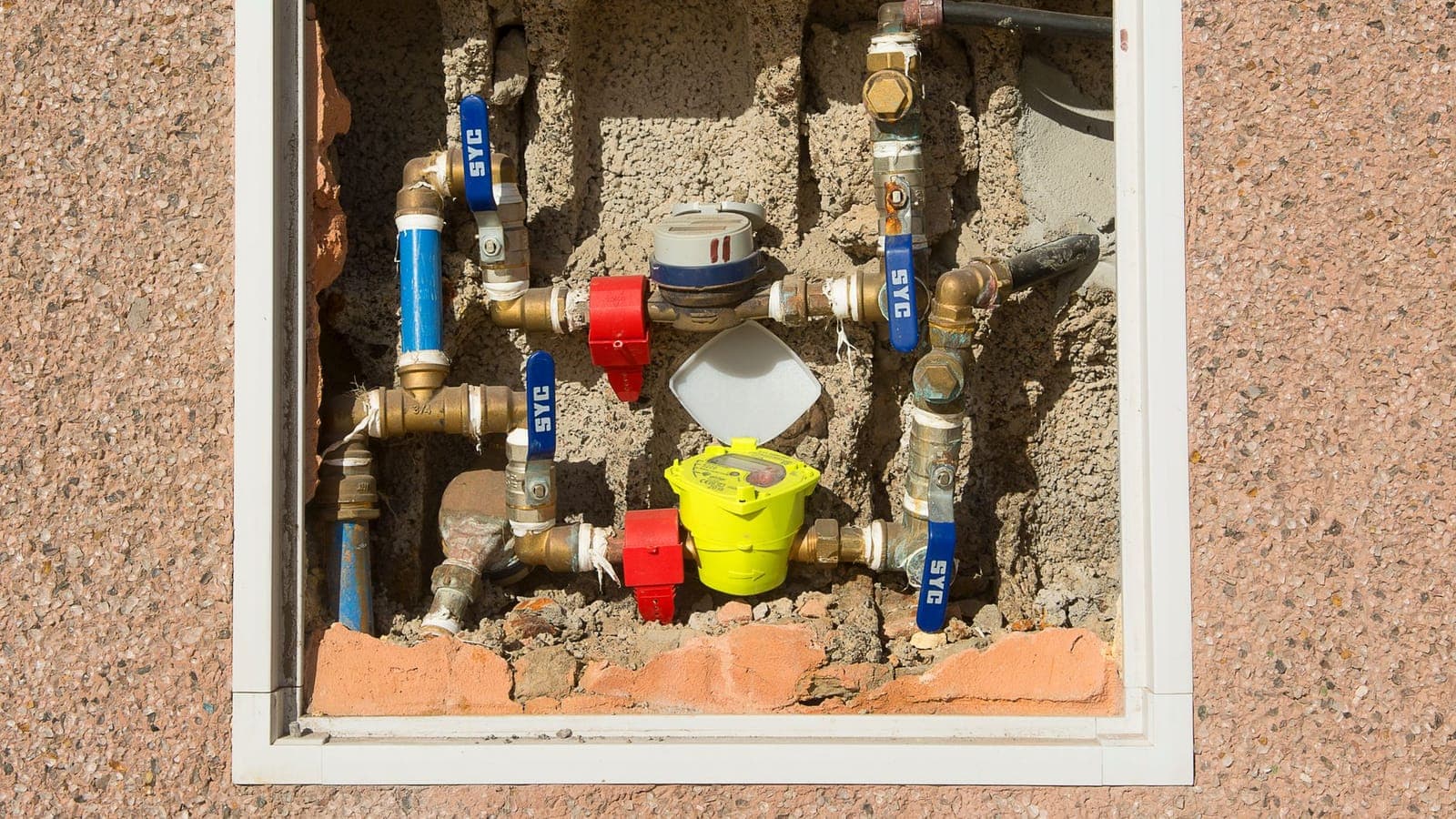 Armario abierto en un muro con el contador de agua, varias llaves de corte de latón y los tubos a la vista