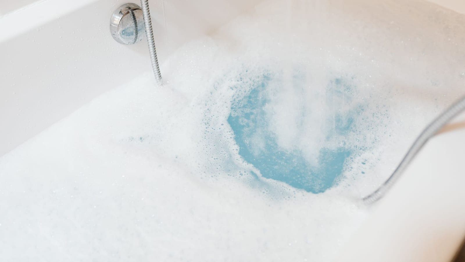 Bañera llenándose de agua y espuma bajo el caño de un monomando cromado con flexible