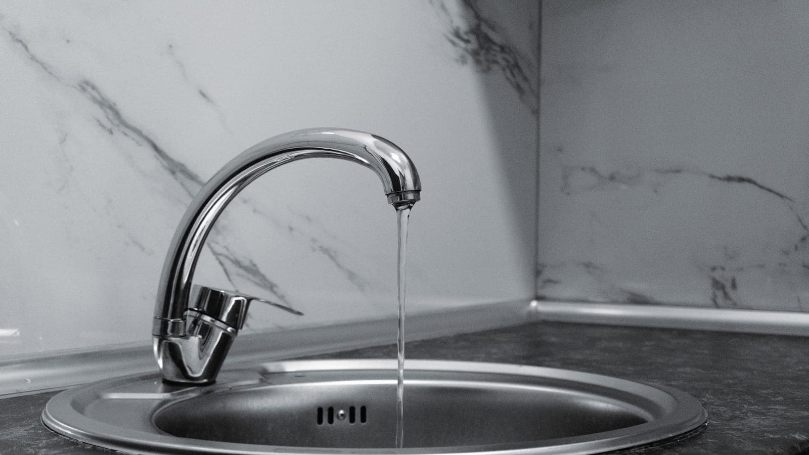 Grifo monomando cromado de fregadero con un hilo de agua cayendo, en blanco y negro