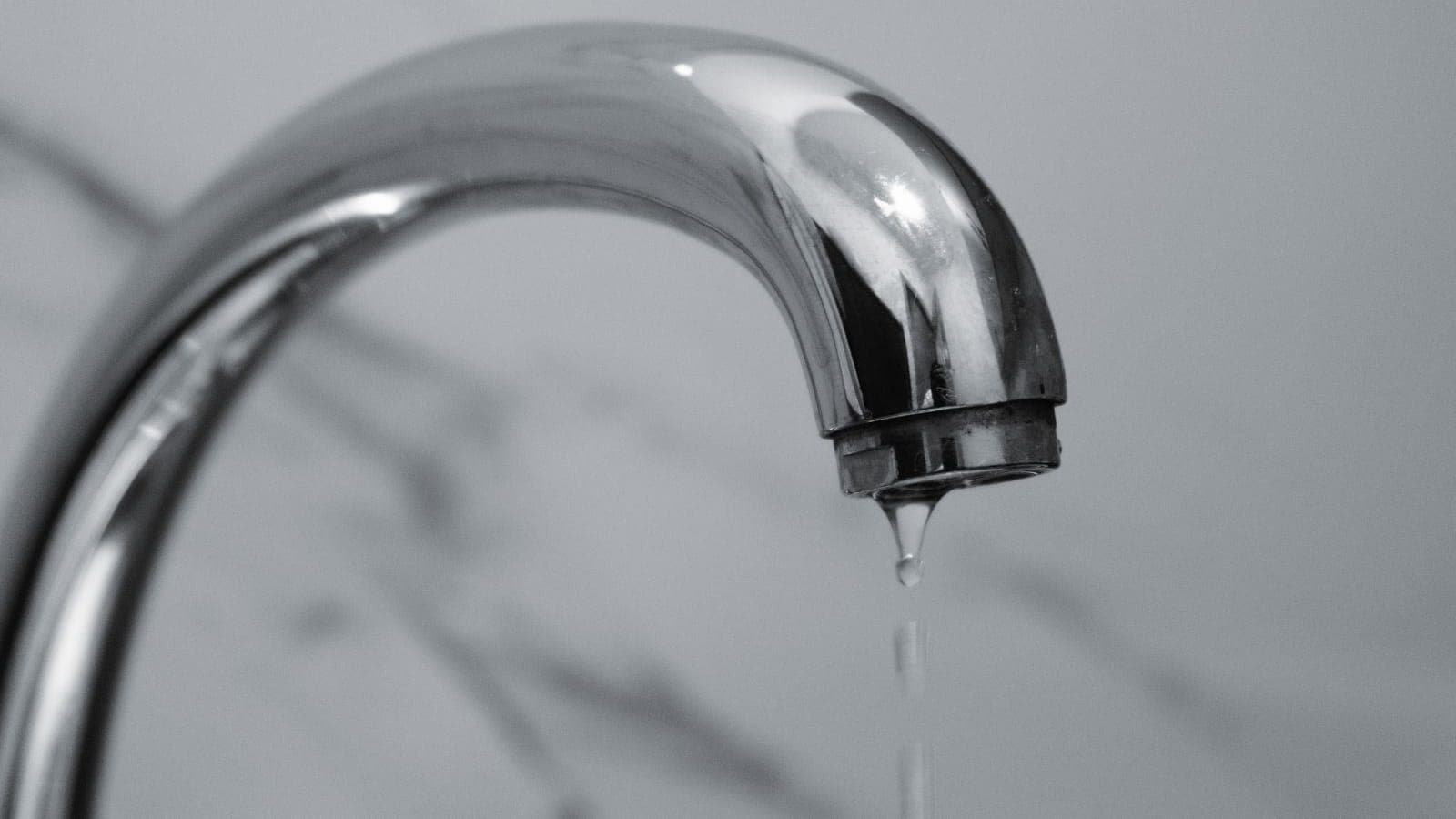 Primer plano en blanco y negro del caño cromado de un grifo con una gota de agua cayendo