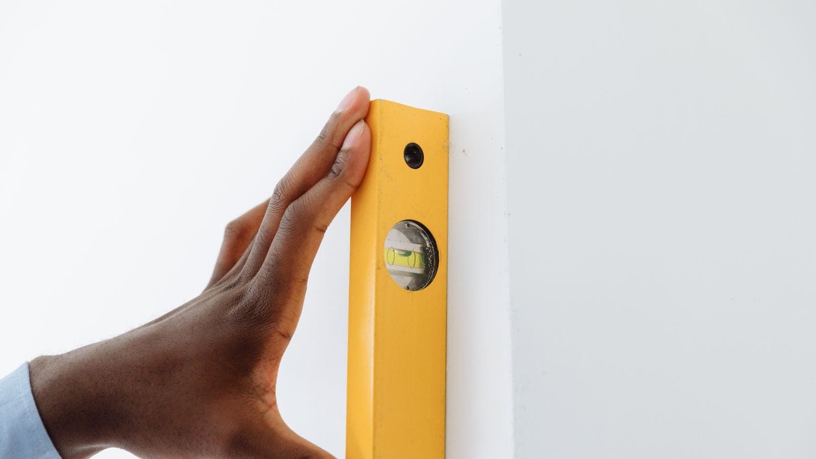 Una mano sujetando un nivel de burbuja amarillo contra el canto de una pared blanca