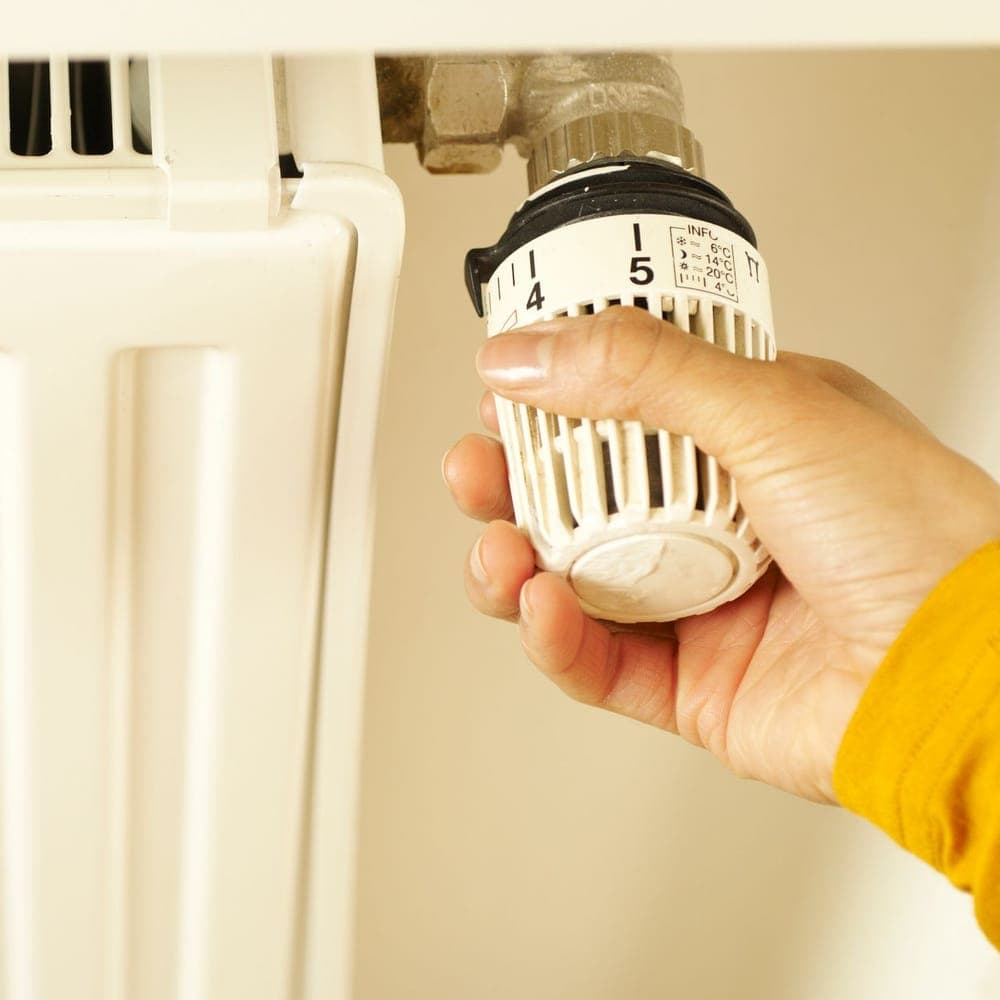 Una mano girando el cabezal termostático blanco de un radiador, con la escala de temperaturas a la vista