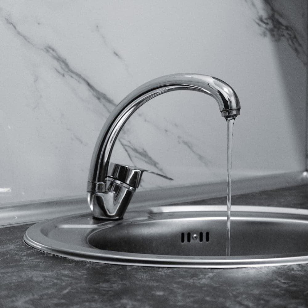 Grifo monomando cromado de fregadero con un hilo de agua cayendo, en blanco y negro
