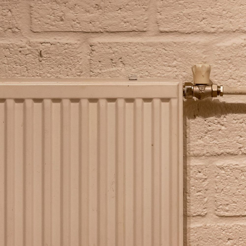 Radiador de panel blanco sobre una pared de ladrillo pintado, con la llave de latón y el tubo a la vista