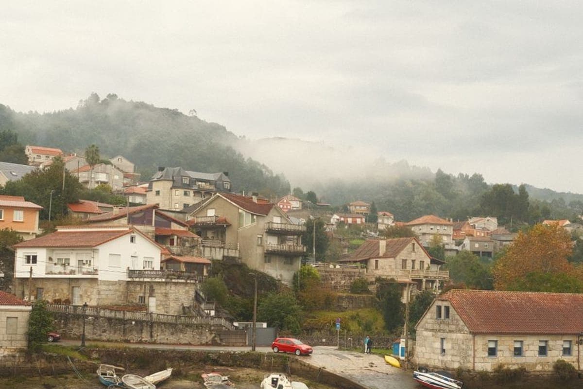 Aldea de casas blancas junto a una ría con las barcas varadas en la marea baja y niebla sobre el monte