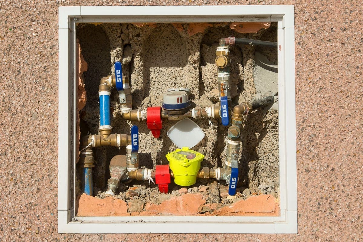 Armario abierto en un muro con el contador de agua, varias llaves de corte de latón y los tubos a la vista