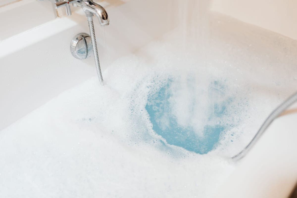 Bañera llenándose de agua y espuma bajo el caño de un monomando cromado con flexible