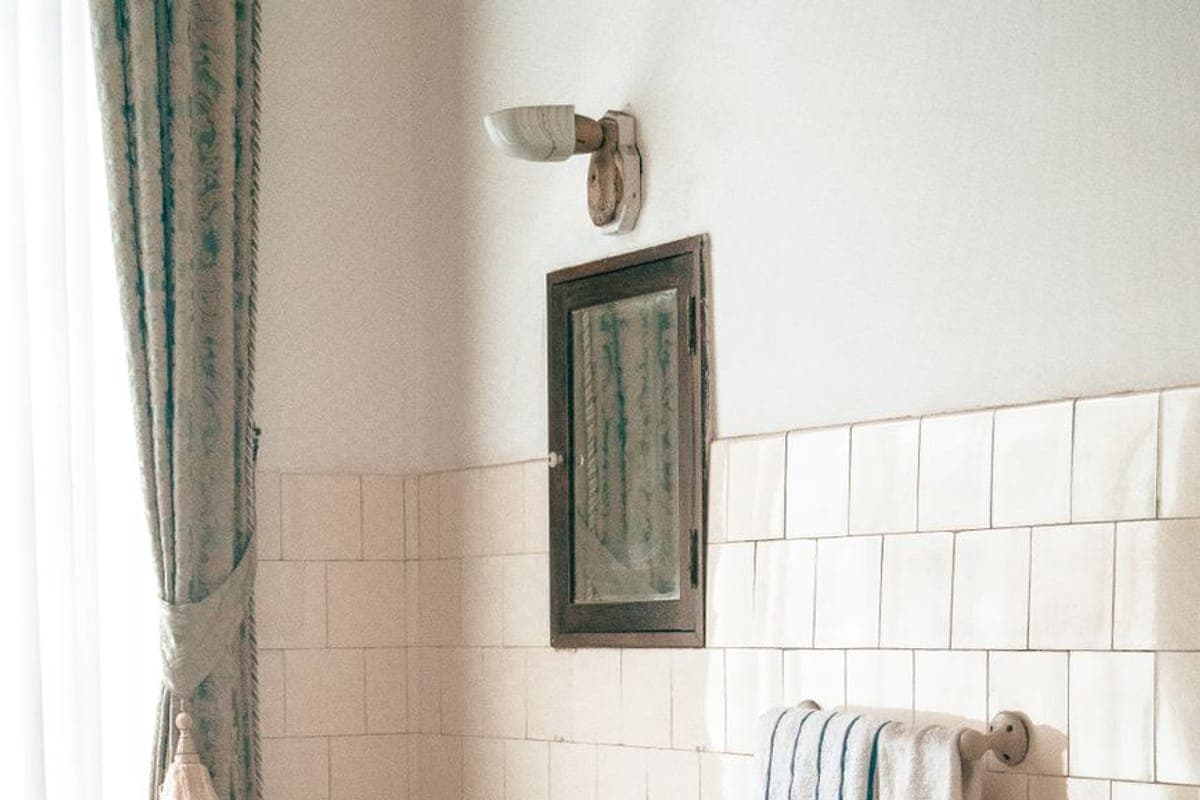 Baño antiguo con azulejo blanco a media altura, lavabo de porcelana con dos grifos, radiador de hierro y suelo de mosaico