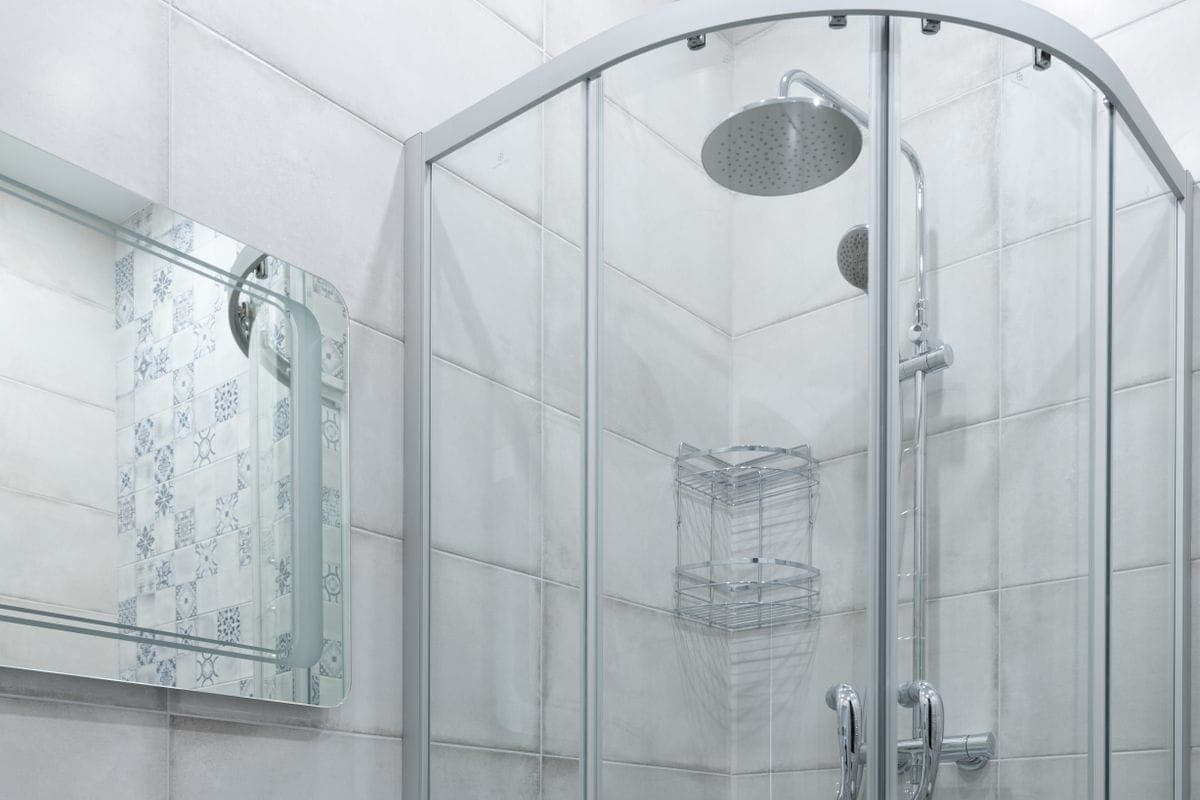 Baño claro con lavabo sobre mueble blanco y una mampara de ducha curva de ángulo con alcachofa de lluvia y grifo termostático