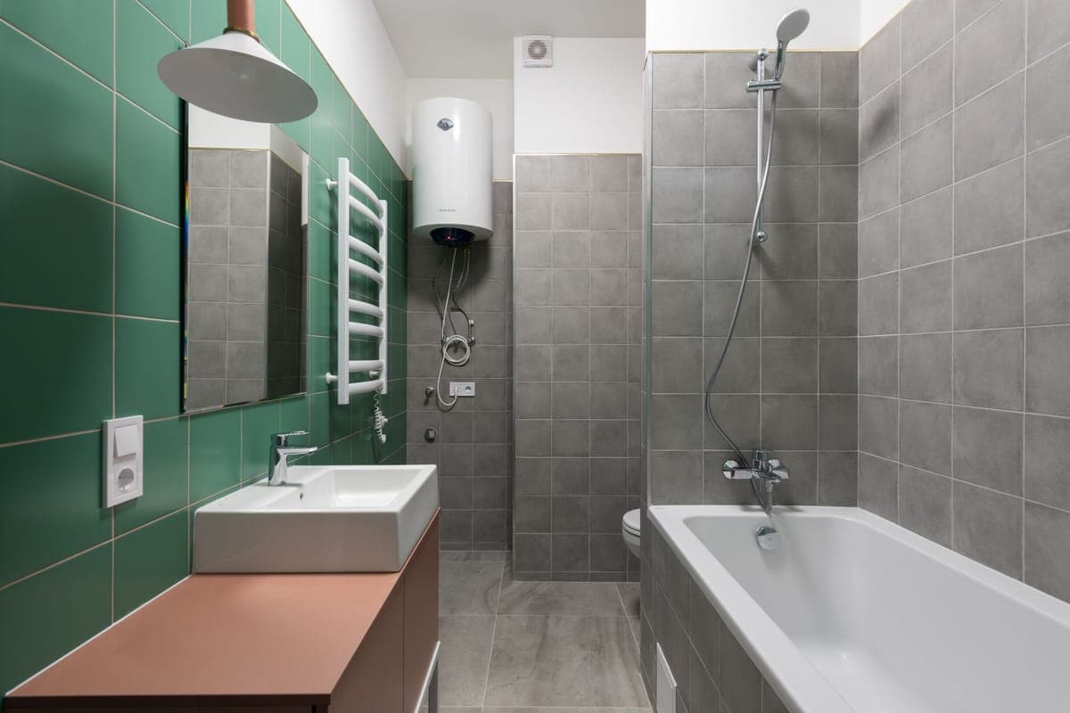 Termo eléctrico blanco colgado en alto en un baño de azulejo verde, junto a la bañera y el lavabo