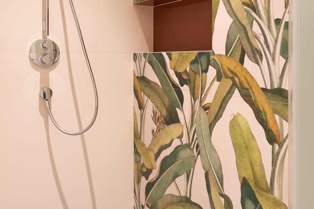 Rincón de ducha con grifo termostático cromado y flexible, junto a una pared alicatada con dibujo de hojas verdes y una hornacina