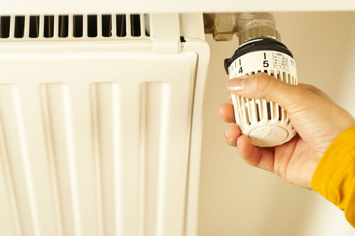 Una mano girando el cabezal termostático blanco de un radiador, con la escala de temperaturas a la vista