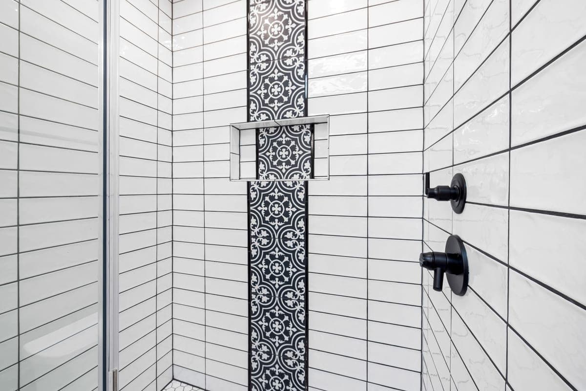 Ducha alicatada de metro blanco con una cenefa vertical de baldosa hidráulica en blanco y negro y una hornacina