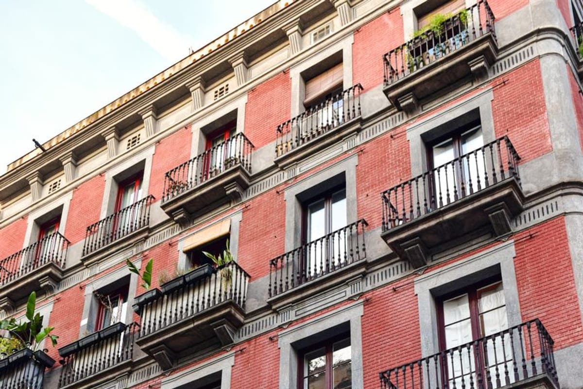 Fachada de ladrillo rojo con balcones de forja, persianas de esterilla y plantas en las barandillas
