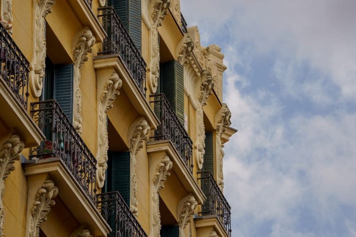Fachada modernista amarilla con ménsulas talladas, balcones de forja y contraventanas verdes