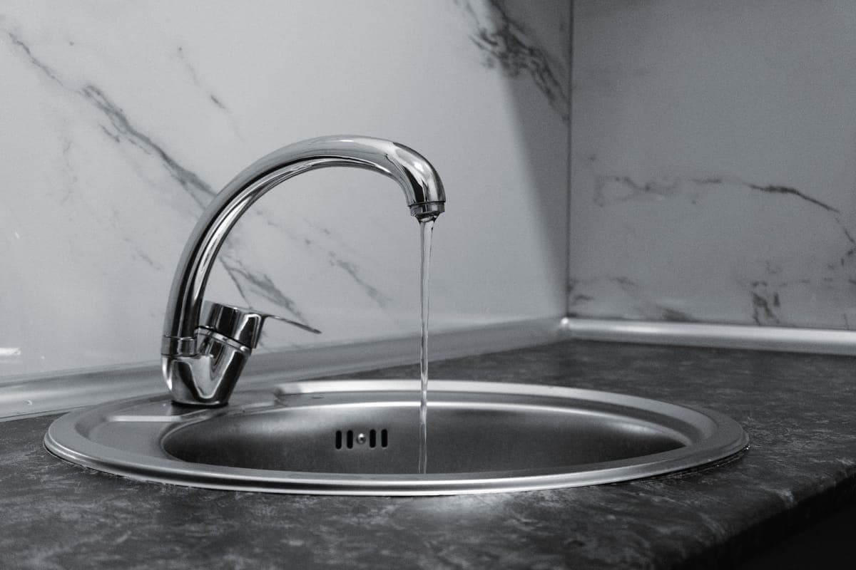 Grifo monomando cromado de fregadero con un hilo de agua cayendo, en blanco y negro