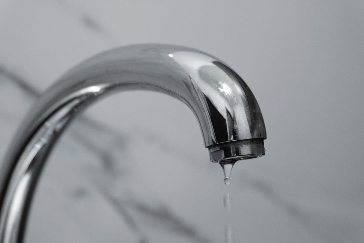 Primer plano en blanco y negro del caño cromado de un grifo con una gota de agua cayendo
