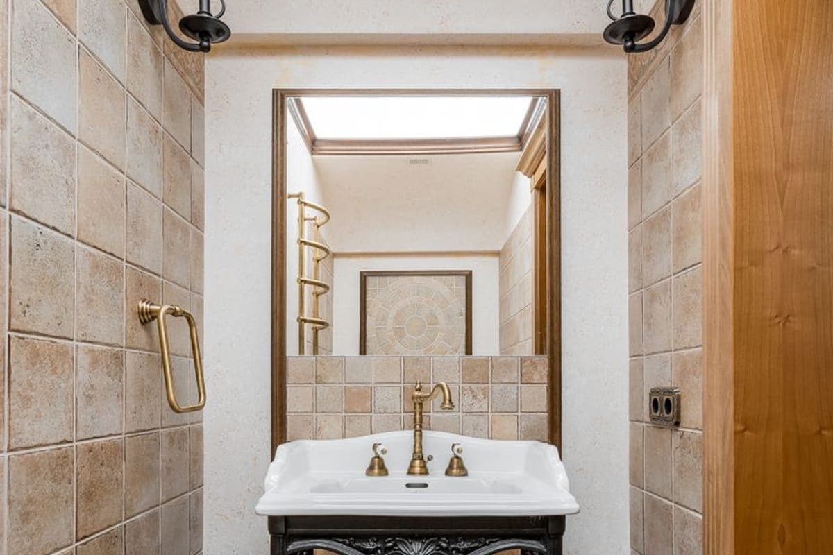 Lavabo de porcelana sobre un pie de hierro fundido, con grifería de latón, espejo y apliques en un aseo alicatado