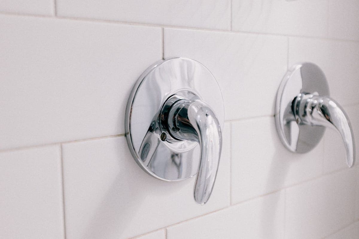 Dos mandos cromados de una grifería empotrada sobre una pared de azulejo blanco