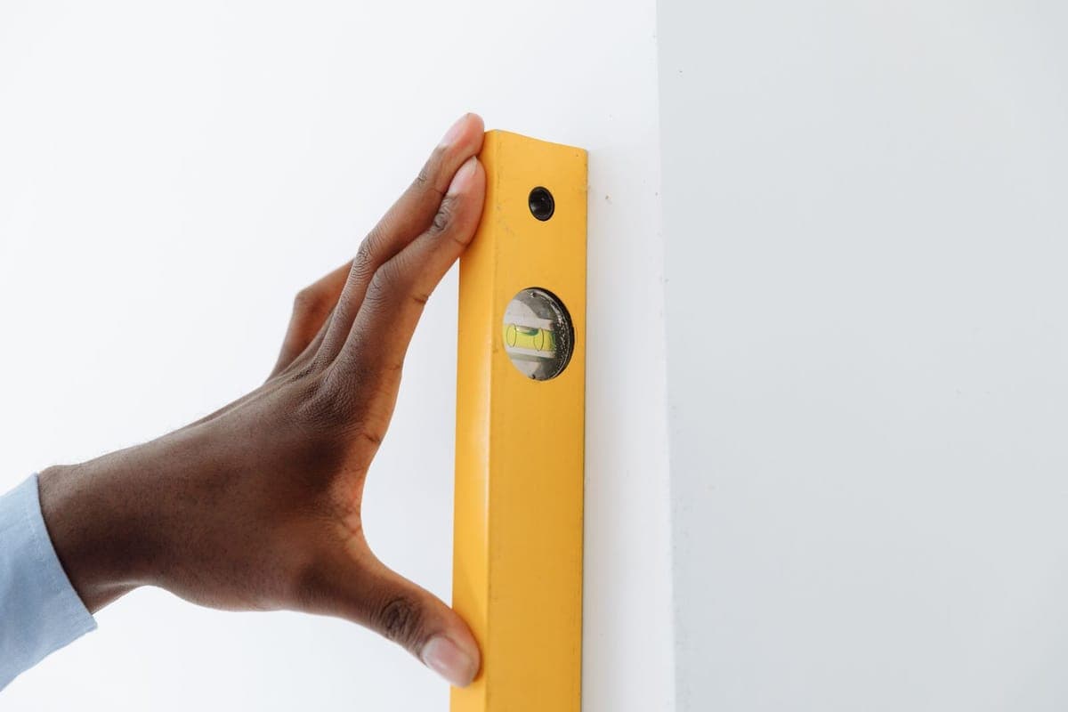 Una mano sujetando un nivel de burbuja amarillo contra el canto de una pared blanca