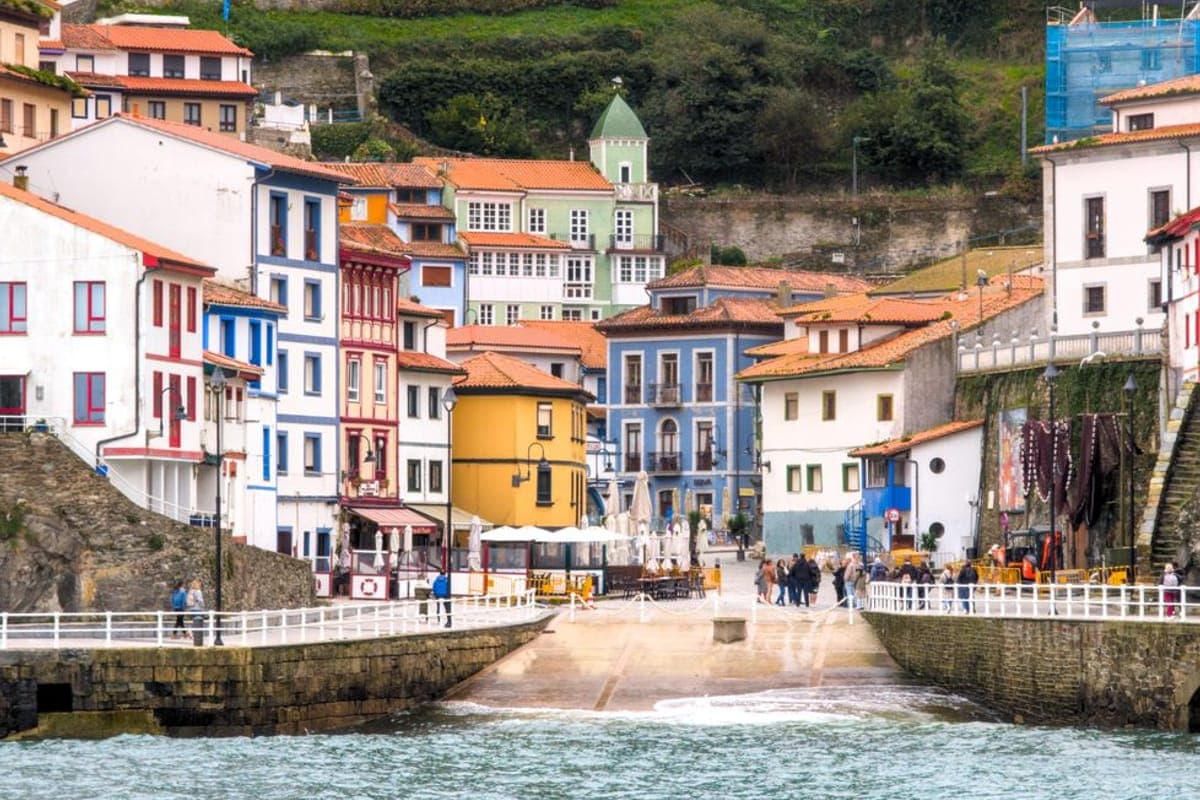 Pueblo marinero de casas de colores escalonadas sobre un puerto, con el agua verde en primer término