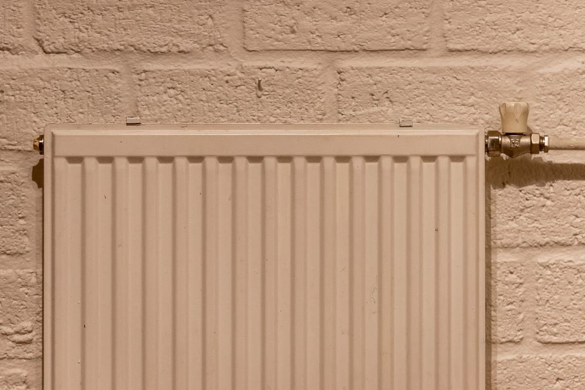 Radiador de panel blanco sobre una pared de ladrillo pintado, con la llave de latón y el tubo a la vista