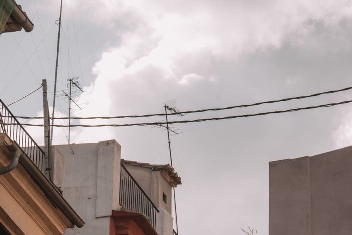 Fachadas y tejados de un casco antiguo con antenas, canalones y balcones de forja bajo un cielo encapotado