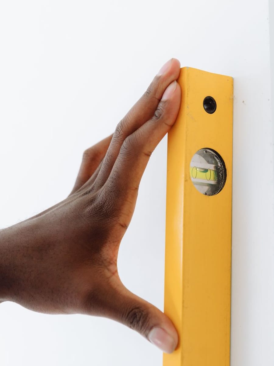 Una mano sujetando un nivel de burbuja amarillo contra el canto de una pared blanca