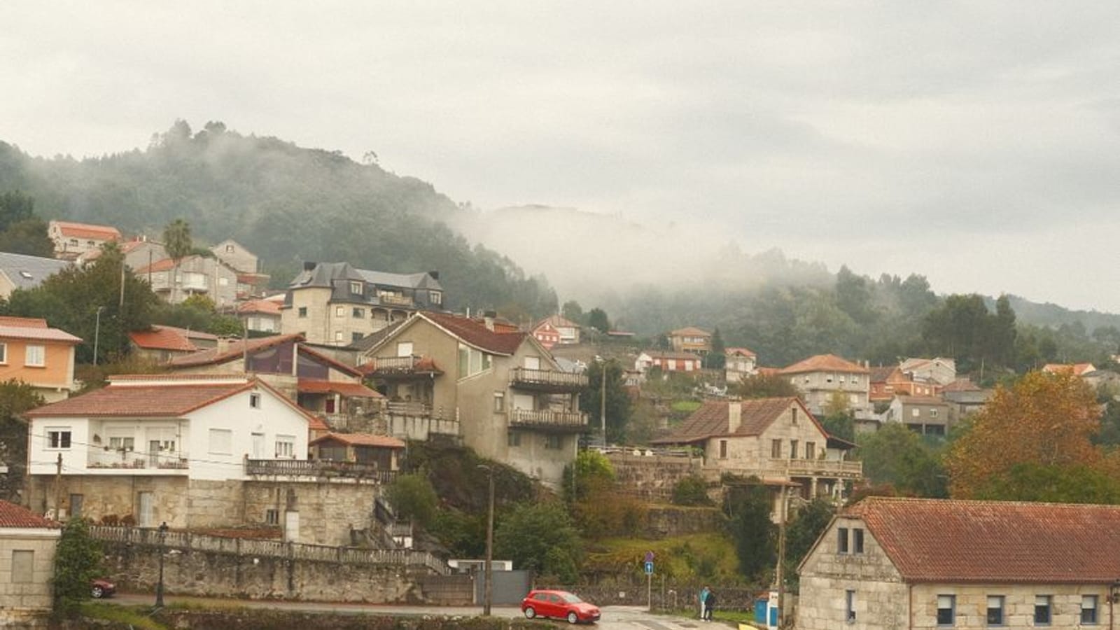 Aldea de casas blancas junto a una ría con las barcas varadas en la marea baja y niebla sobre el monte