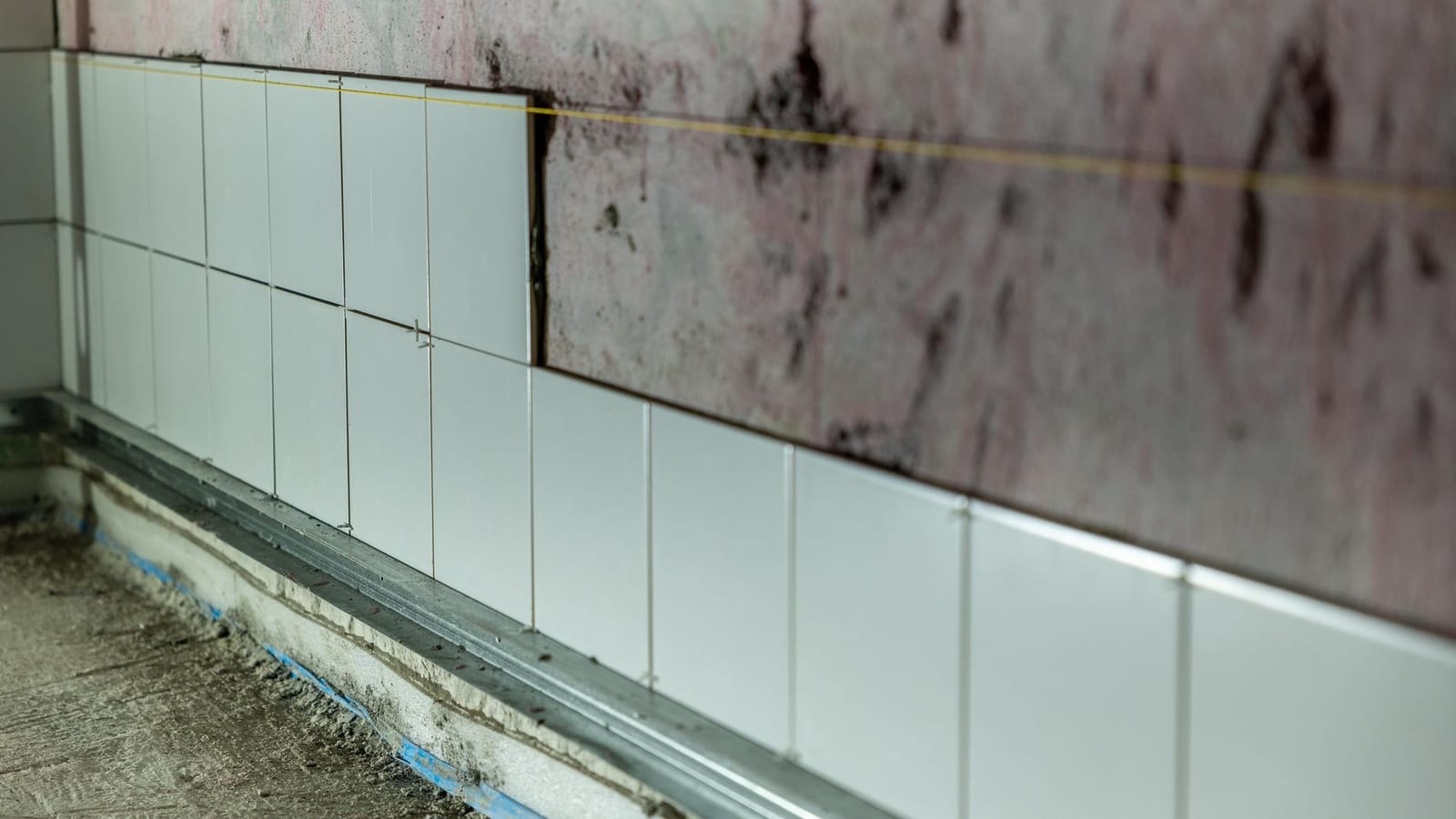 Pared alicatada solo hasta media altura, con crucetas entre las piezas y un hilo tendido como referencia