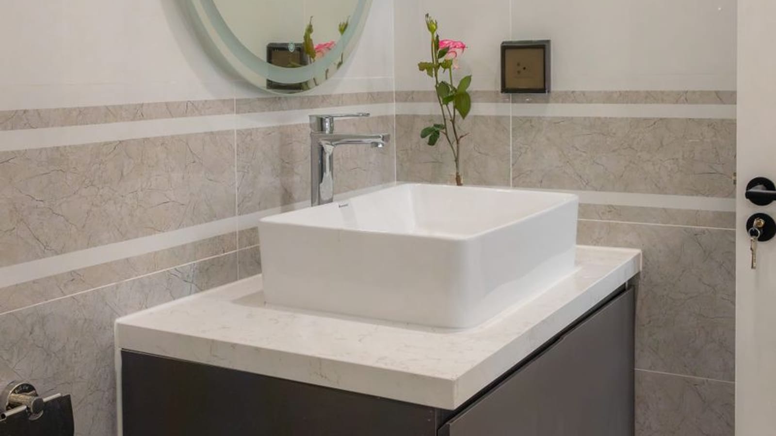 Aseo con lavabo sobre encimera, espejo ovalado iluminado y alicatado de mármol claro