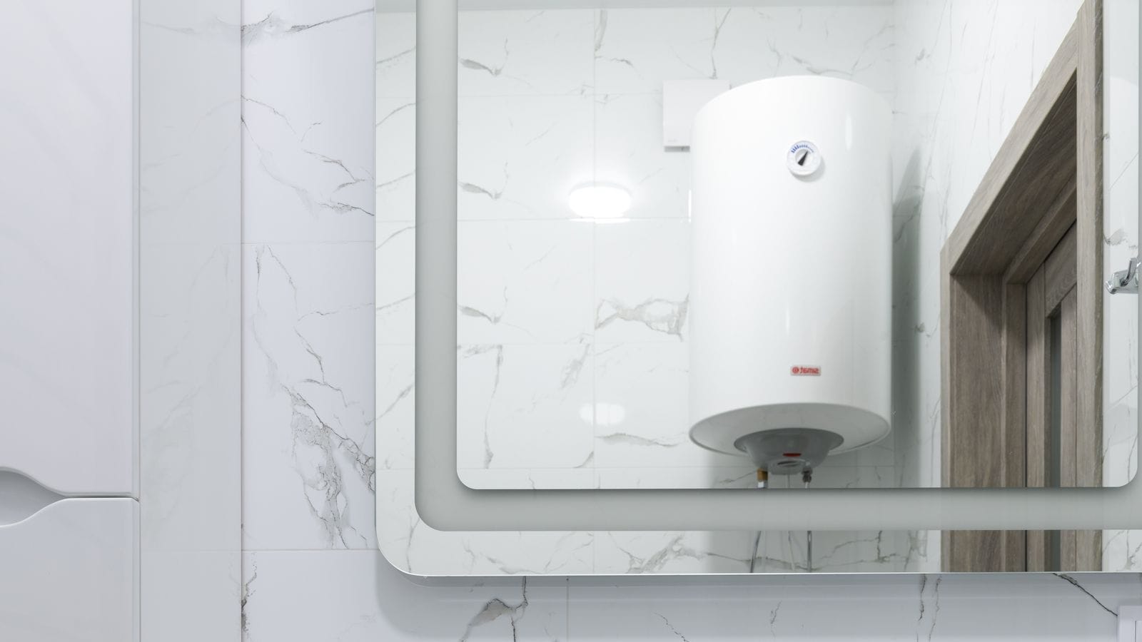 Baño de mármol blanco con un termo eléctrico vertical reflejado en el espejo, sobre el lavabo