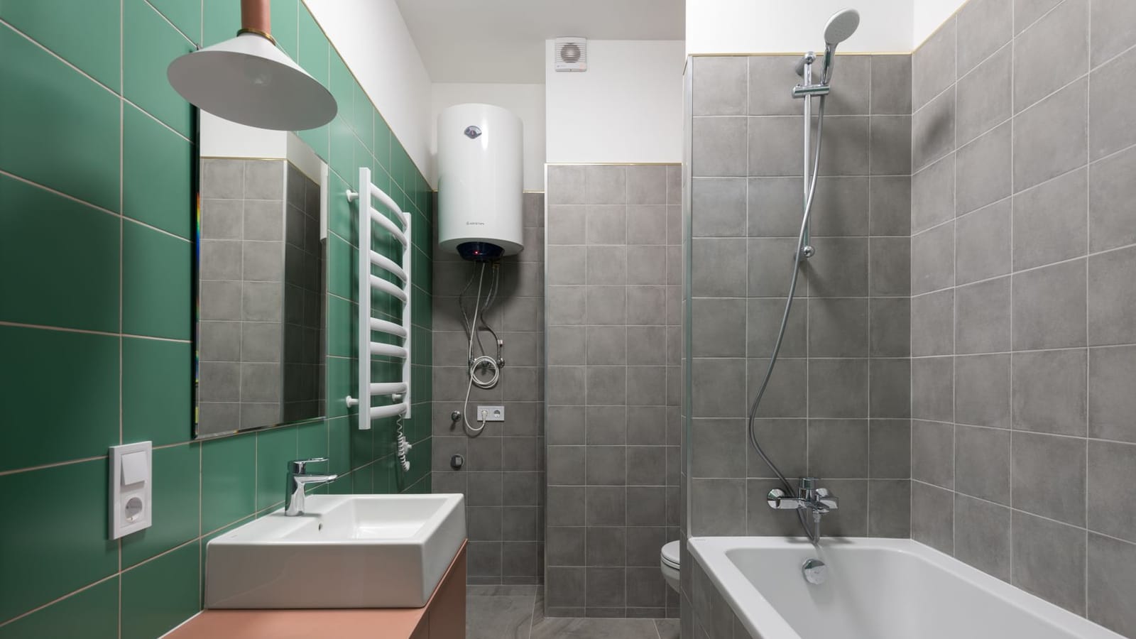 Termo eléctrico blanco colgado en alto en un baño de azulejo verde, junto a la bañera y el lavabo