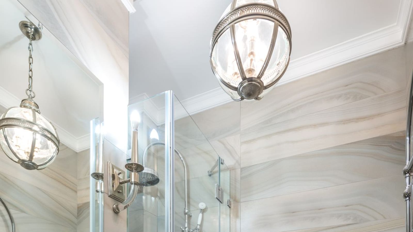 Baño alargado con paredes de azulejo veteado, lavabo sobre mueble blanco, mampara de ducha de cristal e inodoro al fondo