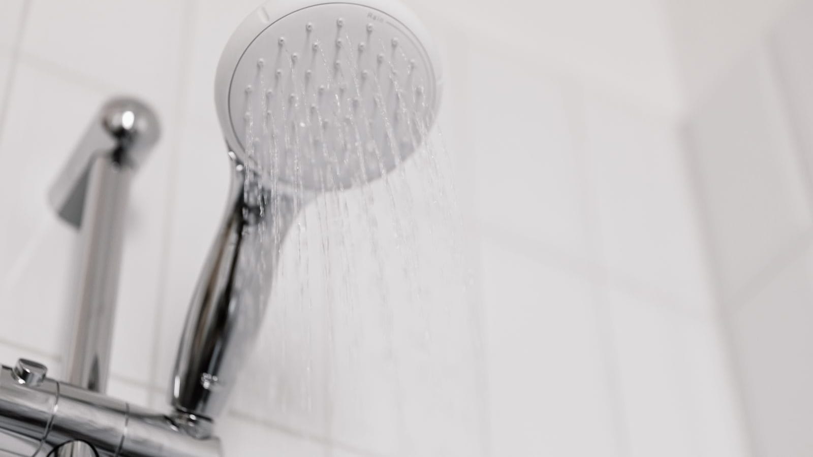 Alcachofa de ducha con el agua cayendo en un baño de azulejo blanco