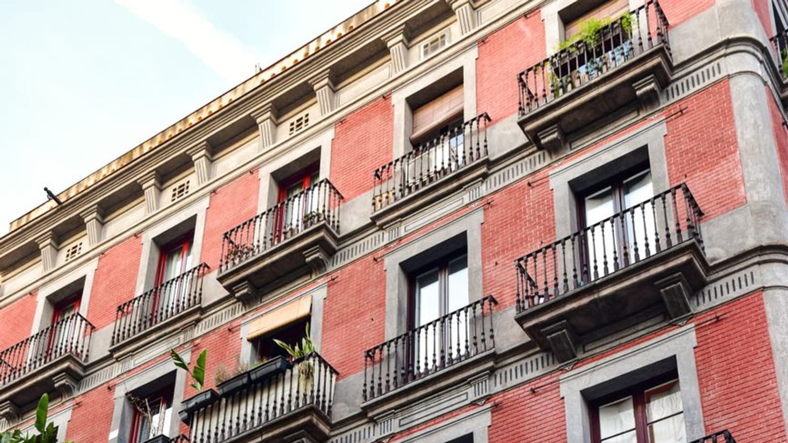Fachada de ladrillo rojo con balcones de forja, persianas de esterilla y plantas en las barandillas