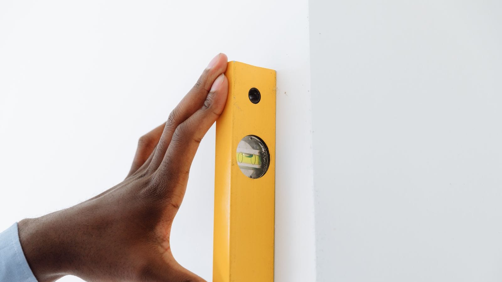Una mano sujetando un nivel de burbuja amarillo contra el canto de una pared blanca