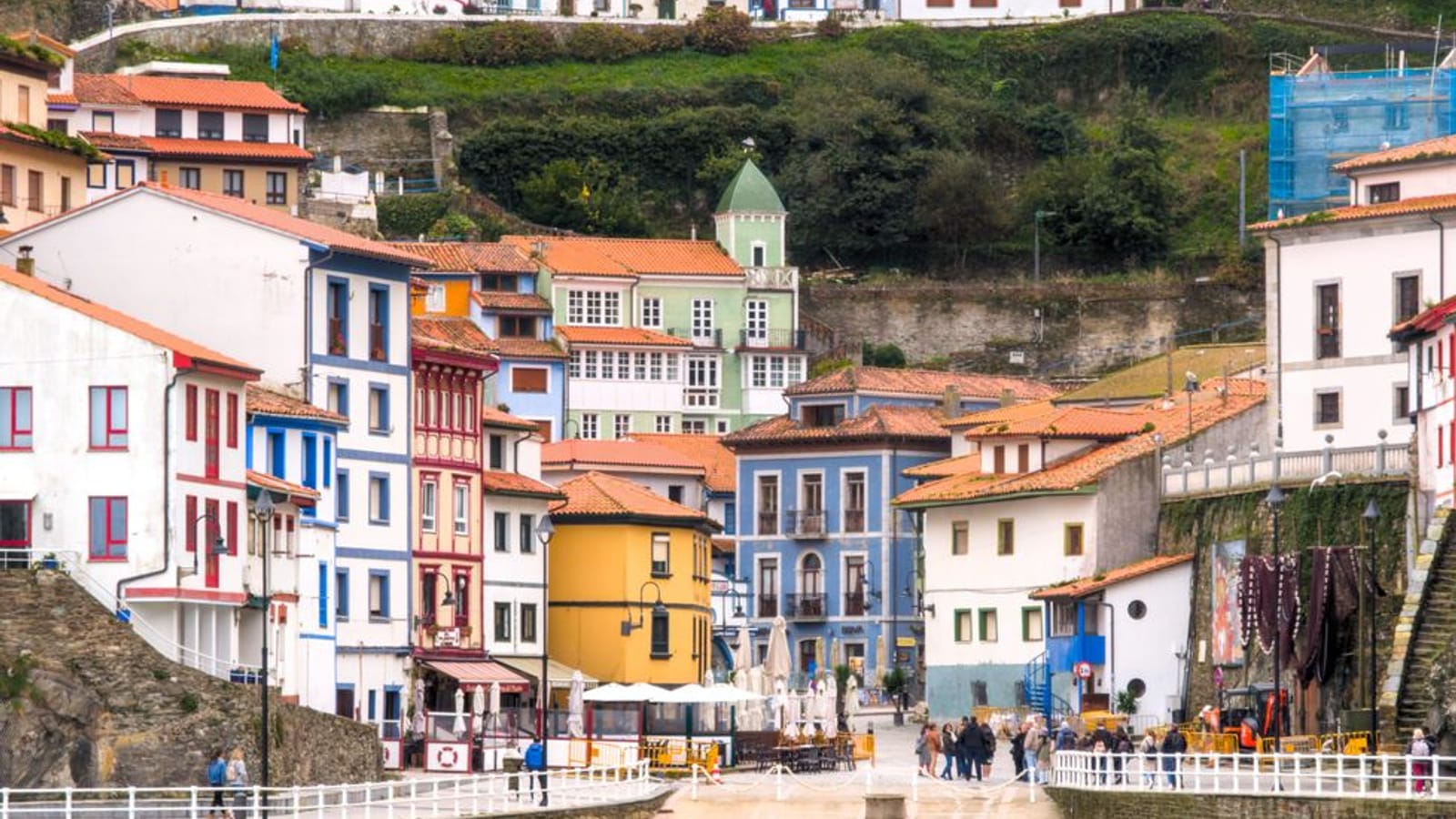 Pueblo marinero de casas de colores escalonadas sobre un puerto, con el agua verde en primer término